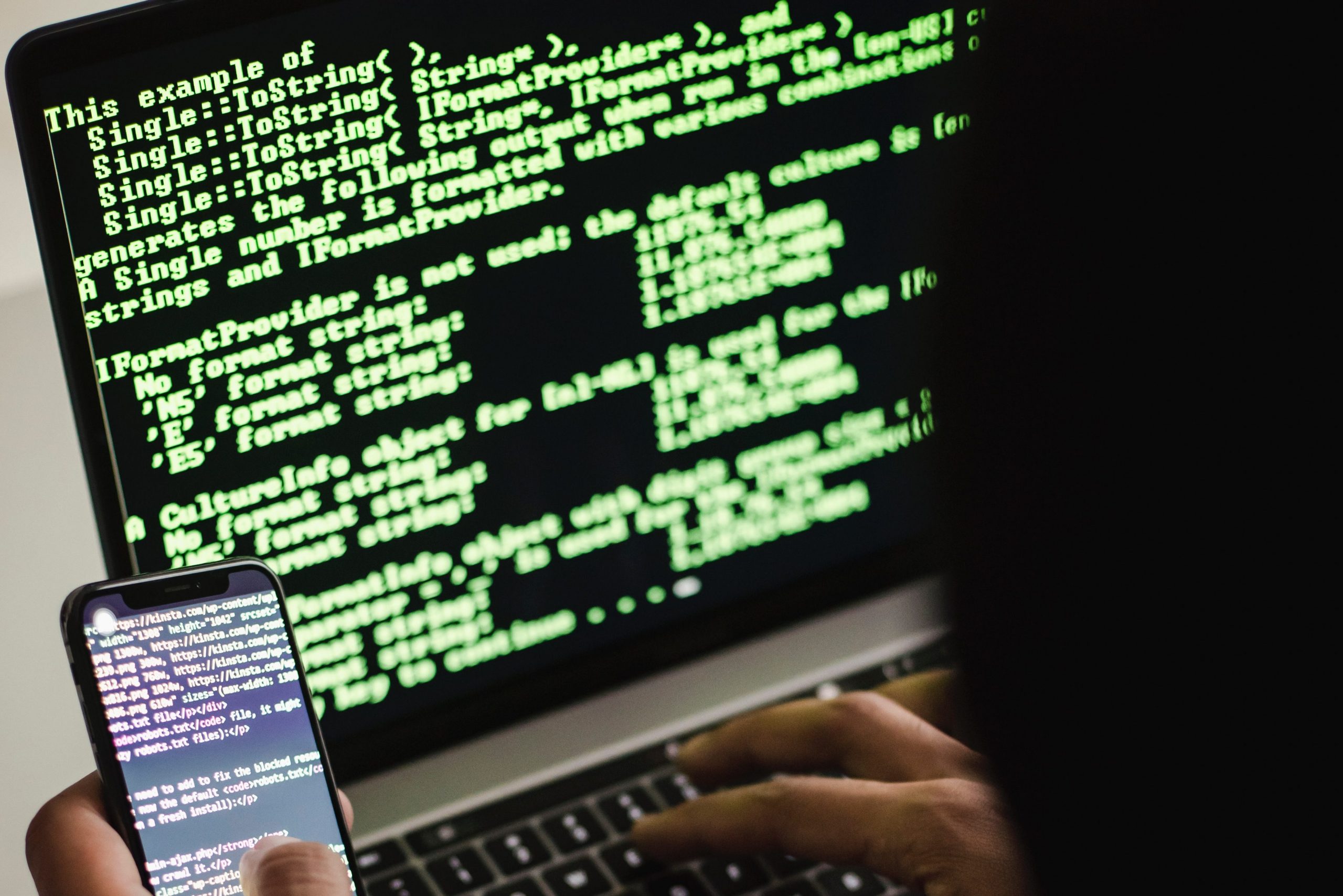 Unidentified person with smartphone typing on laptop